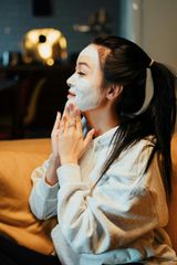 A woman is sitting on a couch with a white mask on her face.