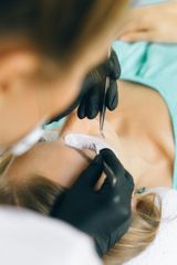 A woman is getting her eyelashes done by a woman wearing black gloves.