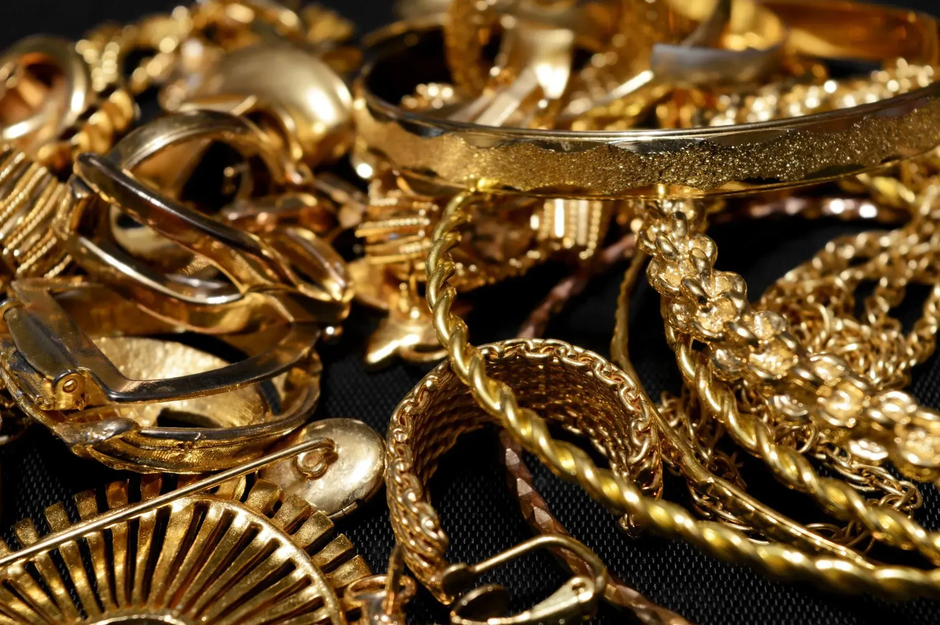 Assorted gold jewelry and chains piled together on a dark background