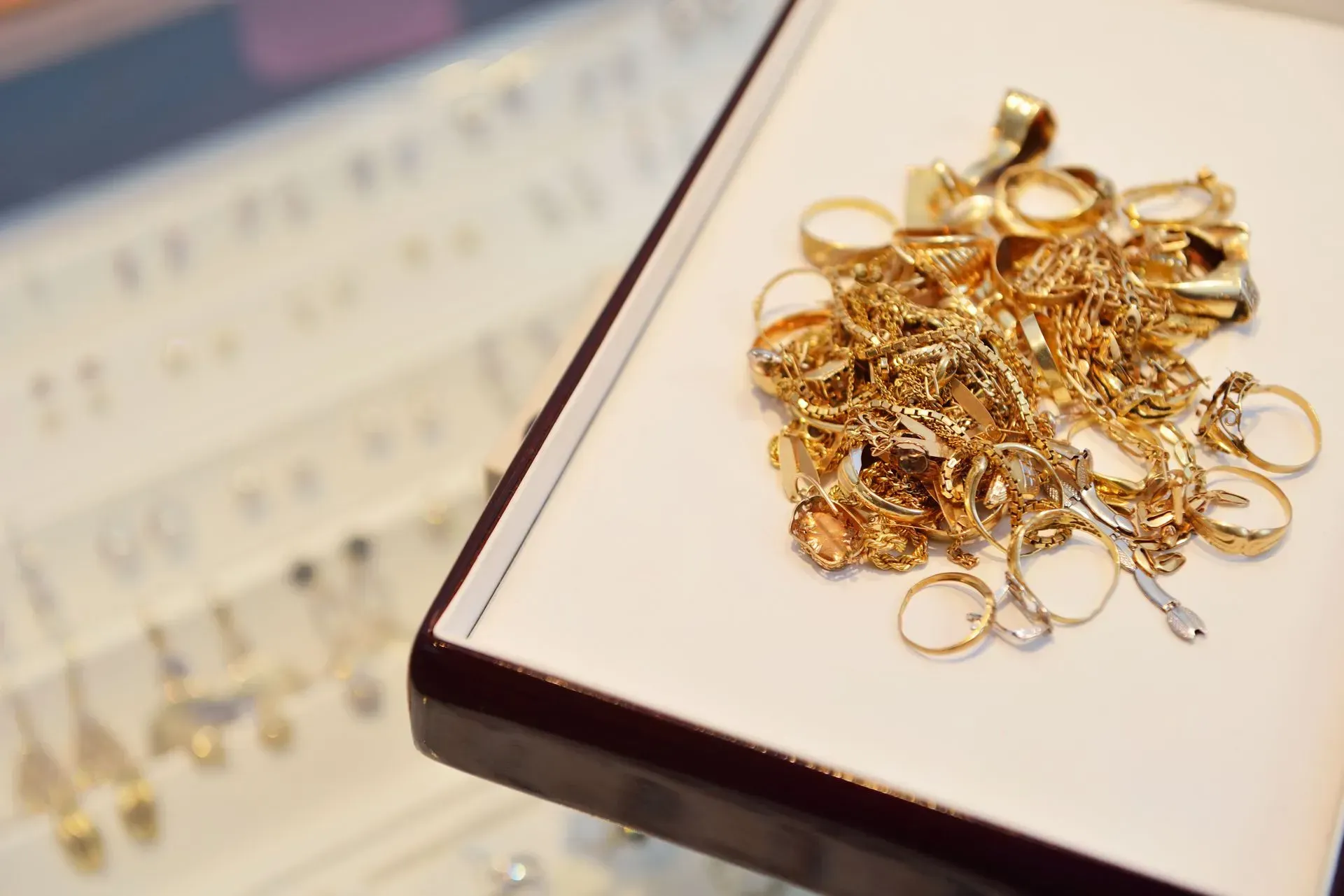 Pile of gold rings on a white tray with blurred jewelry in the background