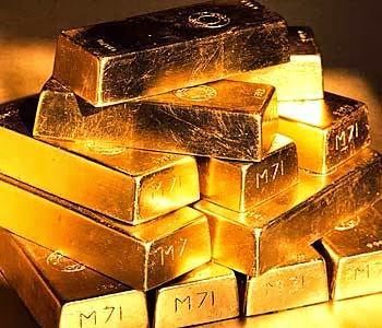 Stacked gold bars shining under warm light, with one darker bar on top.