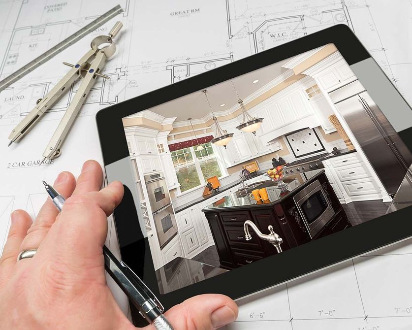 Hand pointing at tablet displaying a kitchen design. Blueprints and drafting tools are on the table.