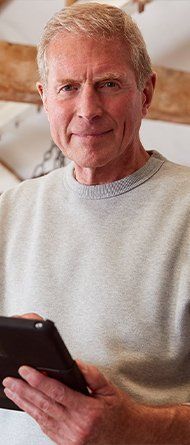A male man smiling into the camera with a electronic tablet in his hand