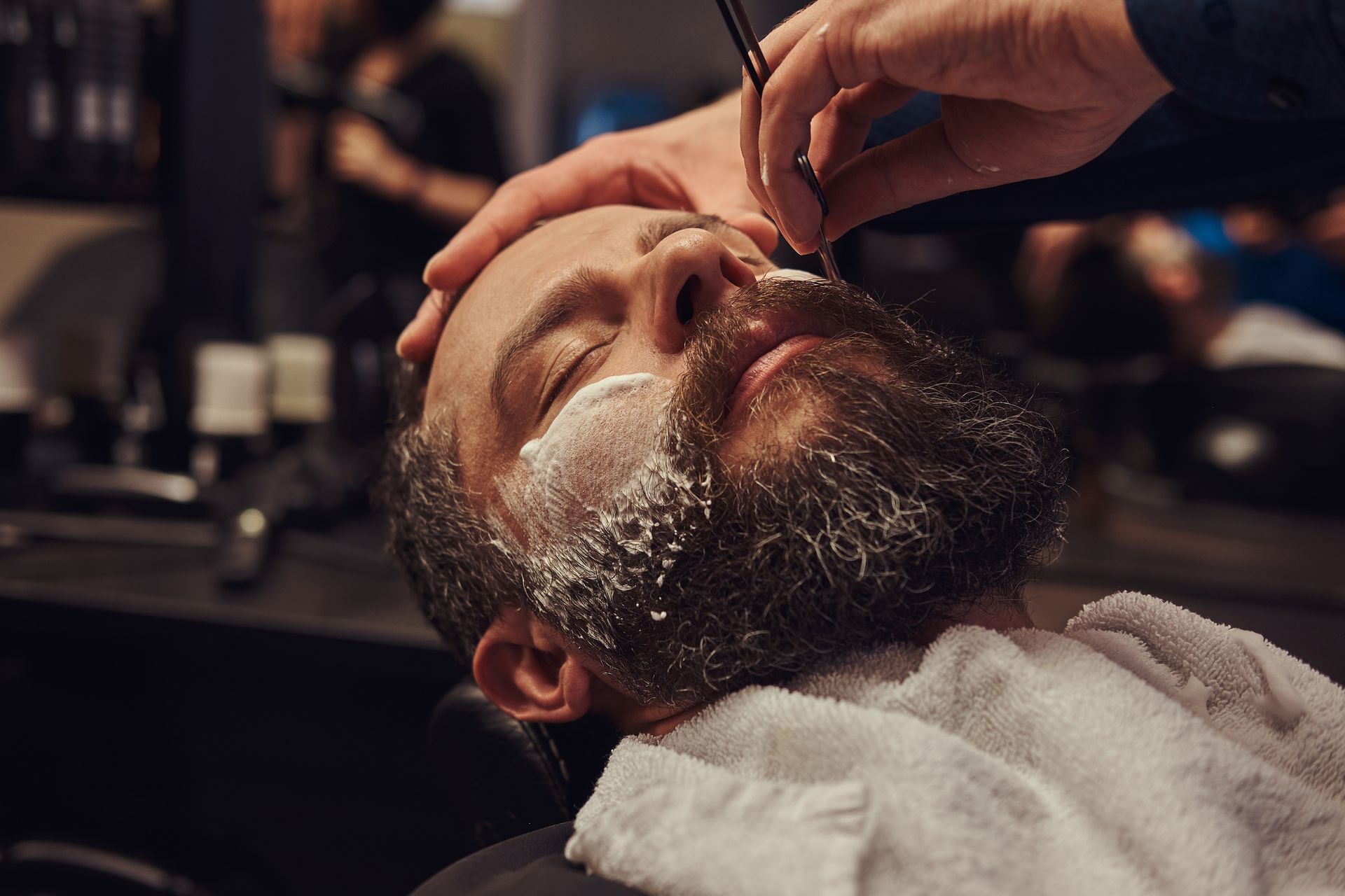 A man is getting his beard shaved at a barber shop.