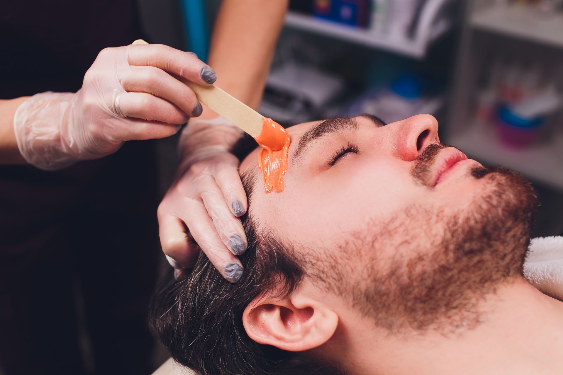 A man is getting his eyebrows waxed in a beauty salon.