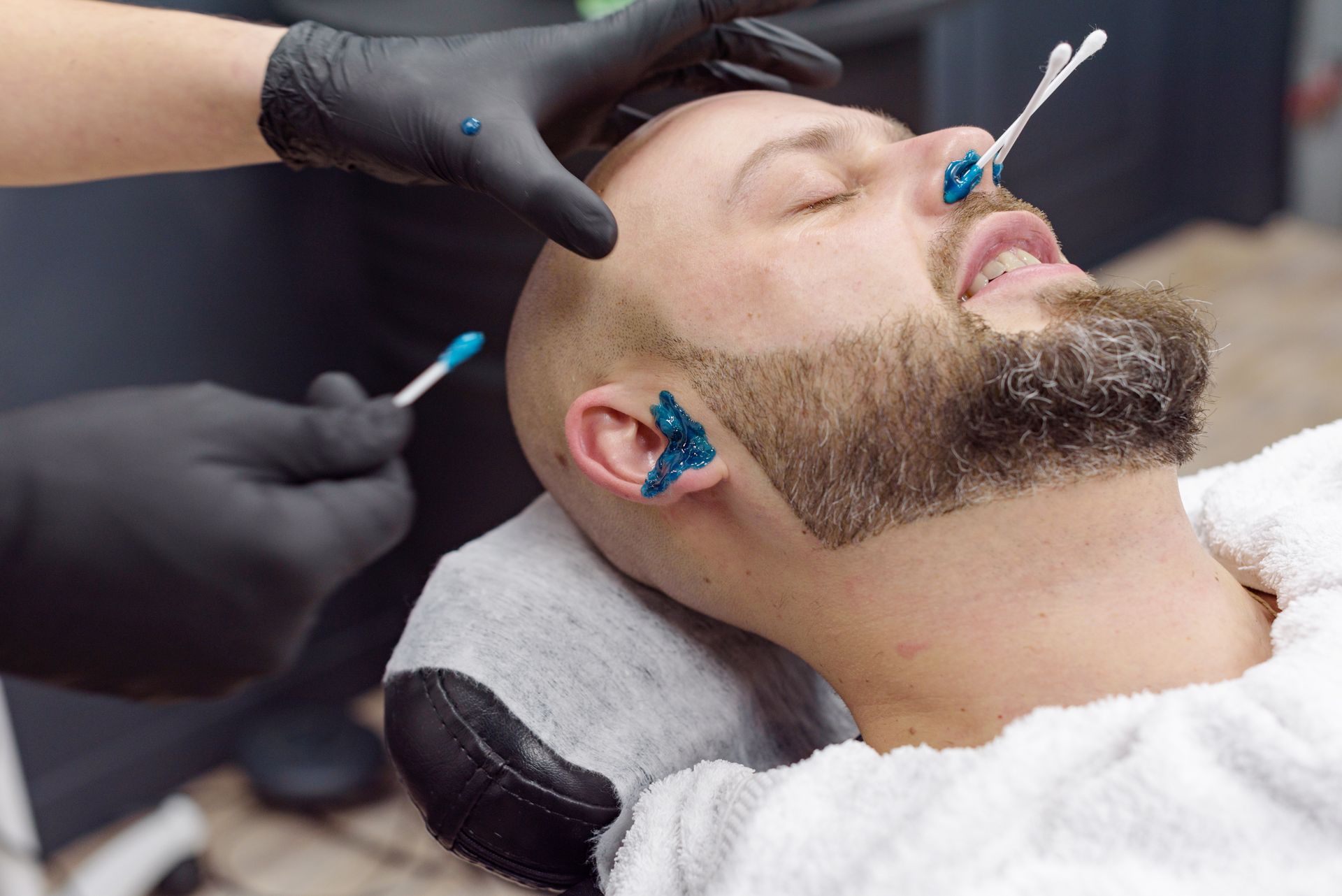 A man with a beard is getting waxed in a barber shop.