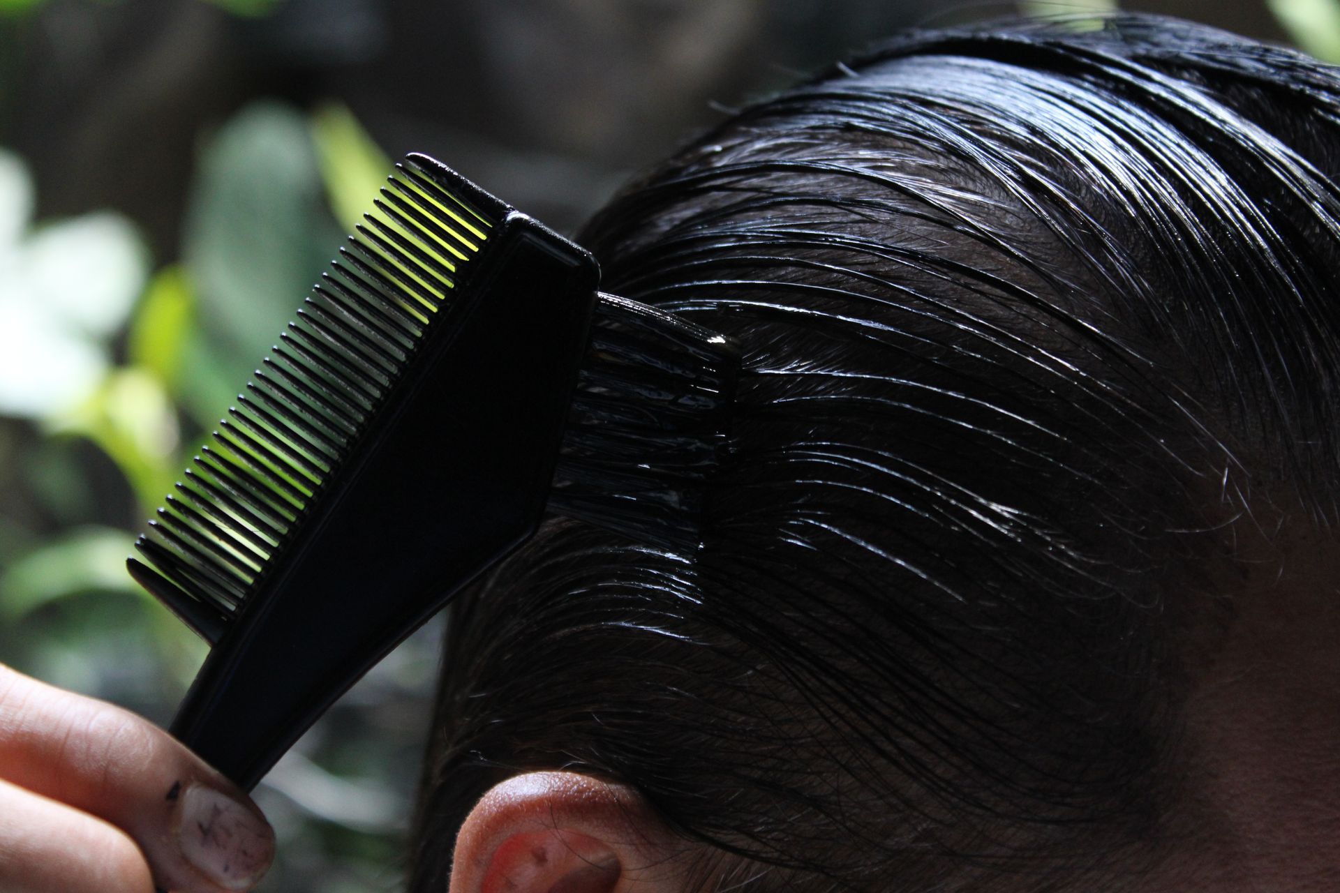 A person combs their hair with a black comb