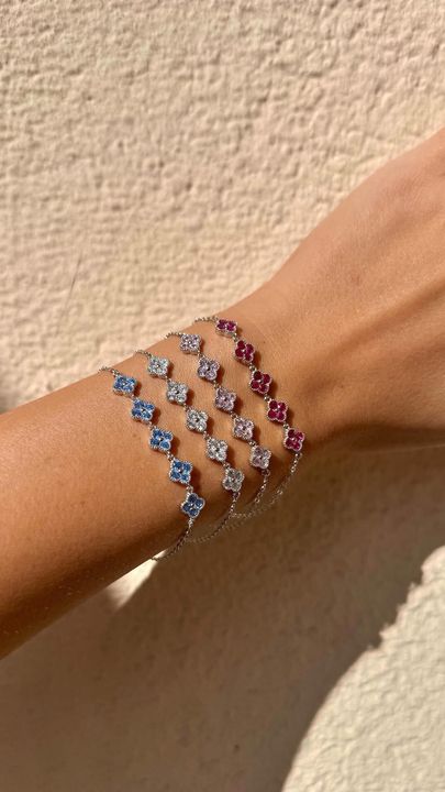 Il polso di una persona è adornato da quattro delicati braccialetti con ciondoli a forma di trifoglio nei toni del rosso, del bianco e del blu.