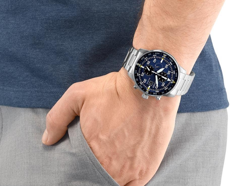 Una persona indossa al polso un orologio cronografo con quadrante blu e cinturino in metallo argentato, mentre tiene la mano in tasca.