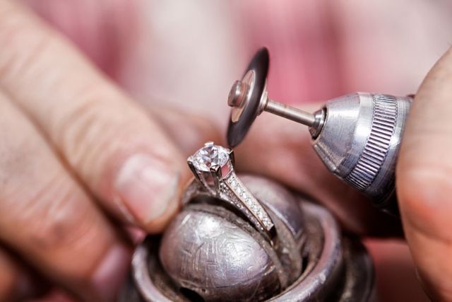 Un gioielliere utilizza un utensile rotante con un piccolo disco lucidante per rifinire un anello di diamanti tenuto in una morsa metallica.