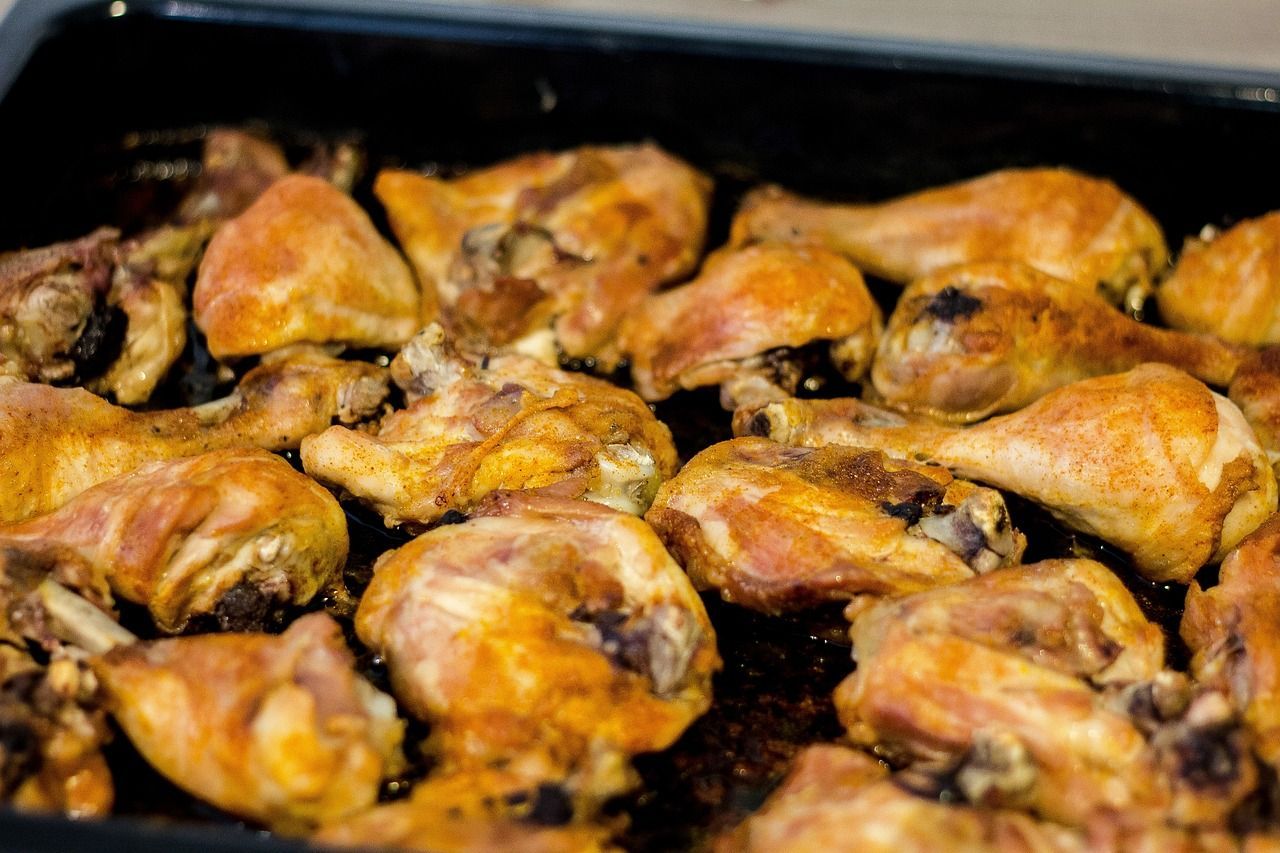 Several baked chicken drumsticks arranged on a dark oven tray, seasoned with spices and cooked to a 