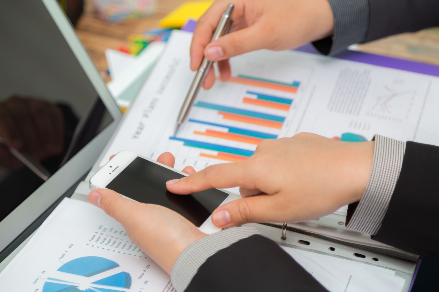 Two business professionals reviewing financial charts and data on a smartphone and paper reports.