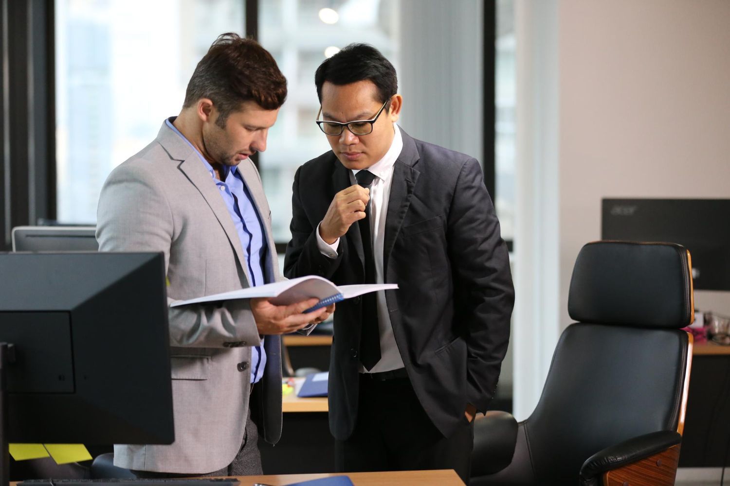 Two professionals in suits reviewing a document together in a modern office.
