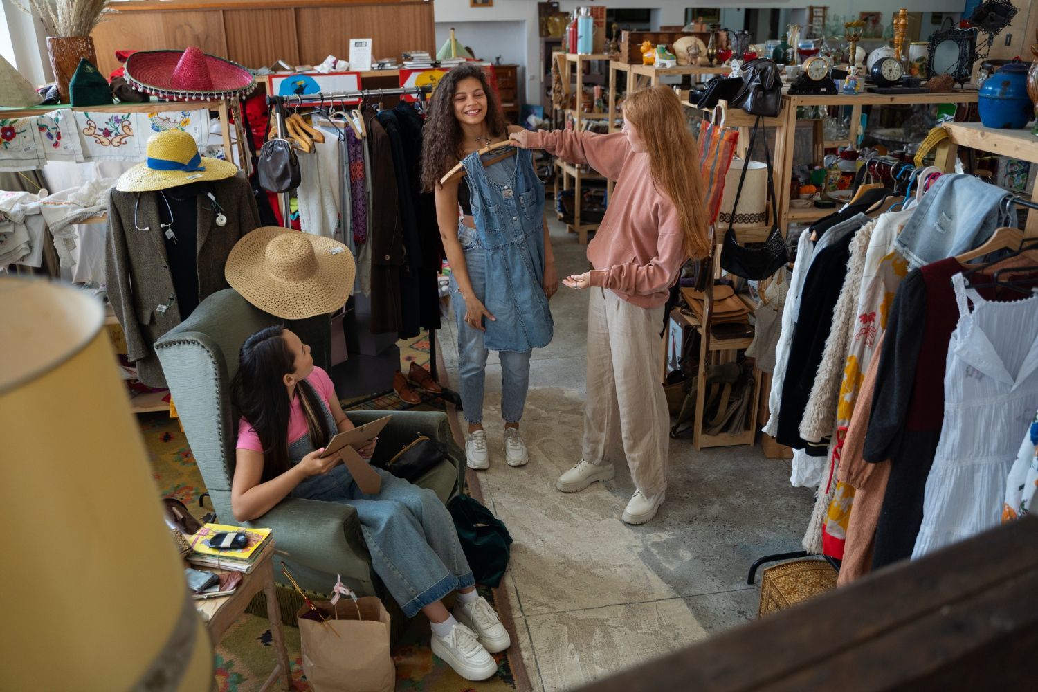 Three people in a cluttered clothing store, with one person seated and two standing while looking at a denim garment.