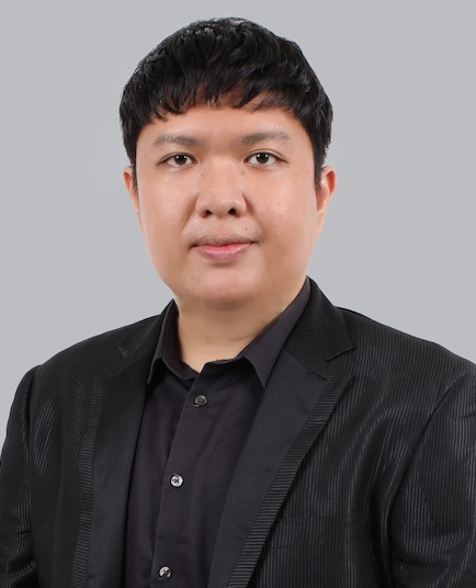 A person with freckles wears a textured yellow top and long green tassel earrings, posed against a stark white wall.