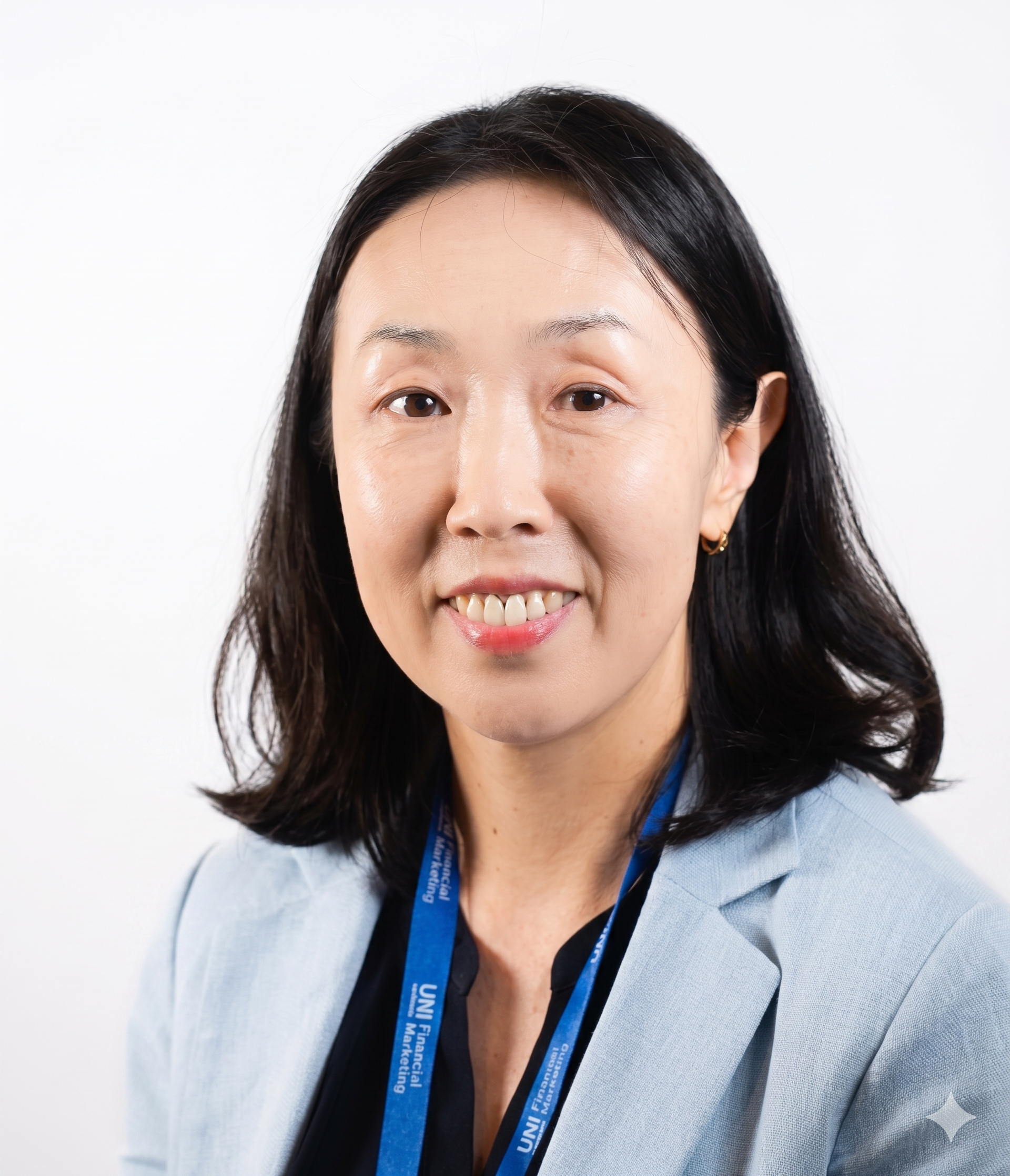A person with freckles wears a textured yellow top and long green tassel earrings, posed against a stark white wall.