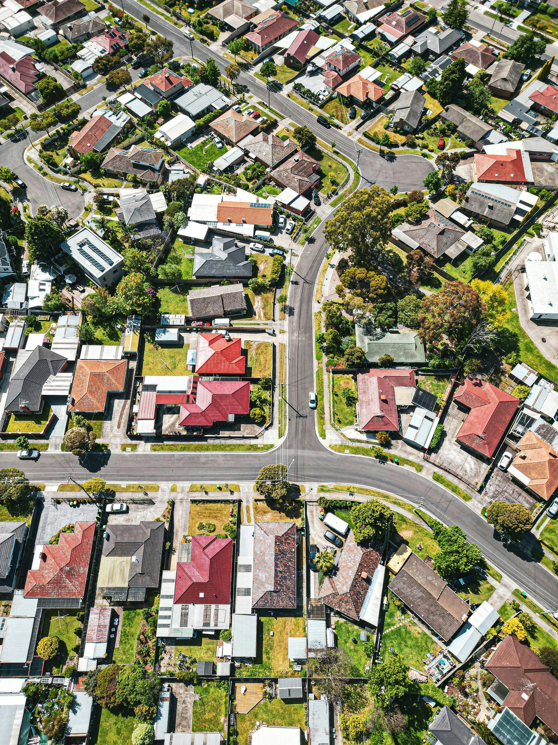 Aerial view of a residential neighborhood with houses featuring red roofs, surrounded by trees and connecting roads.