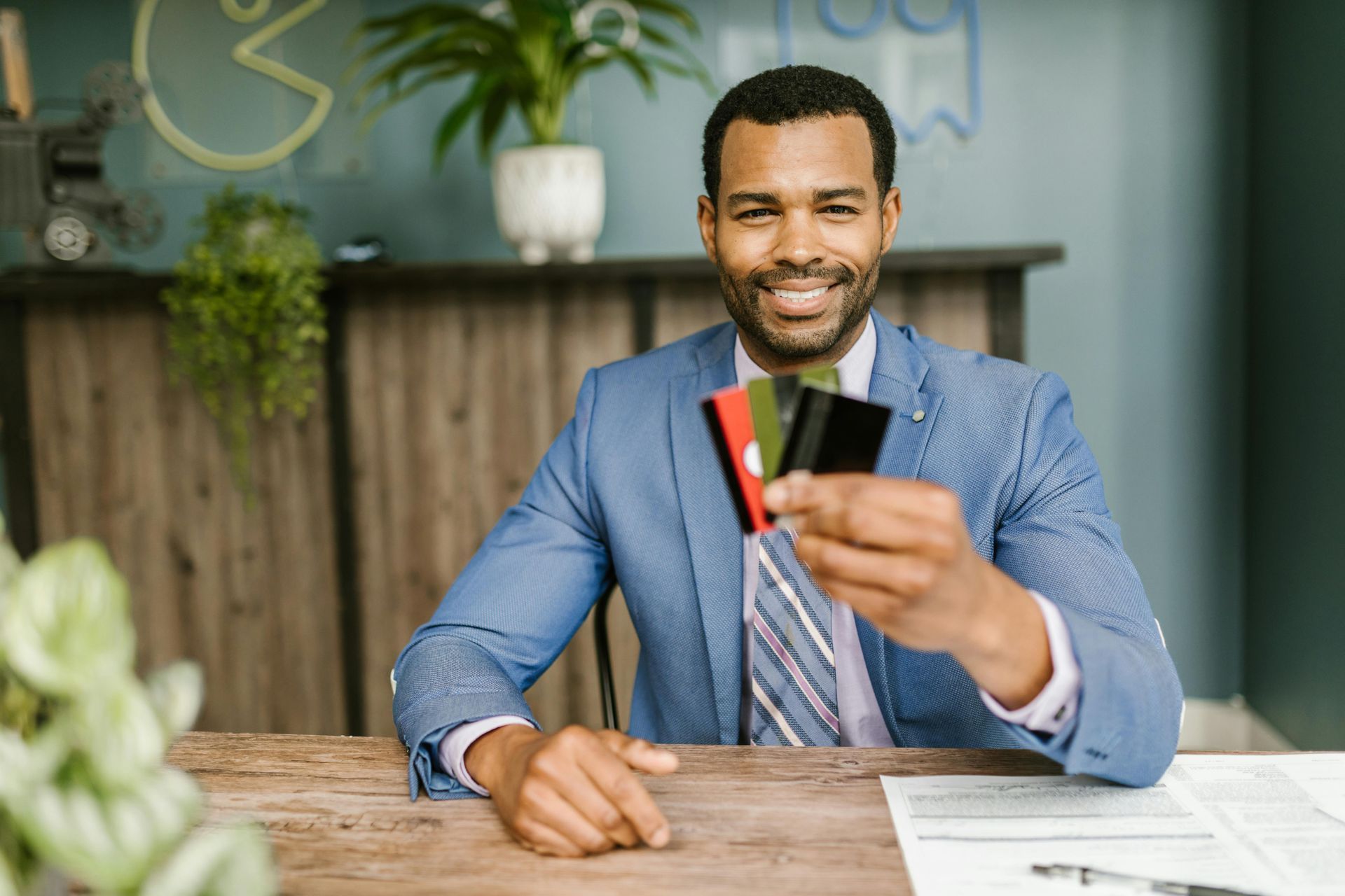 A person in a blue blazer sits at a desk, smiling and holding up a small fan of three credit cards.