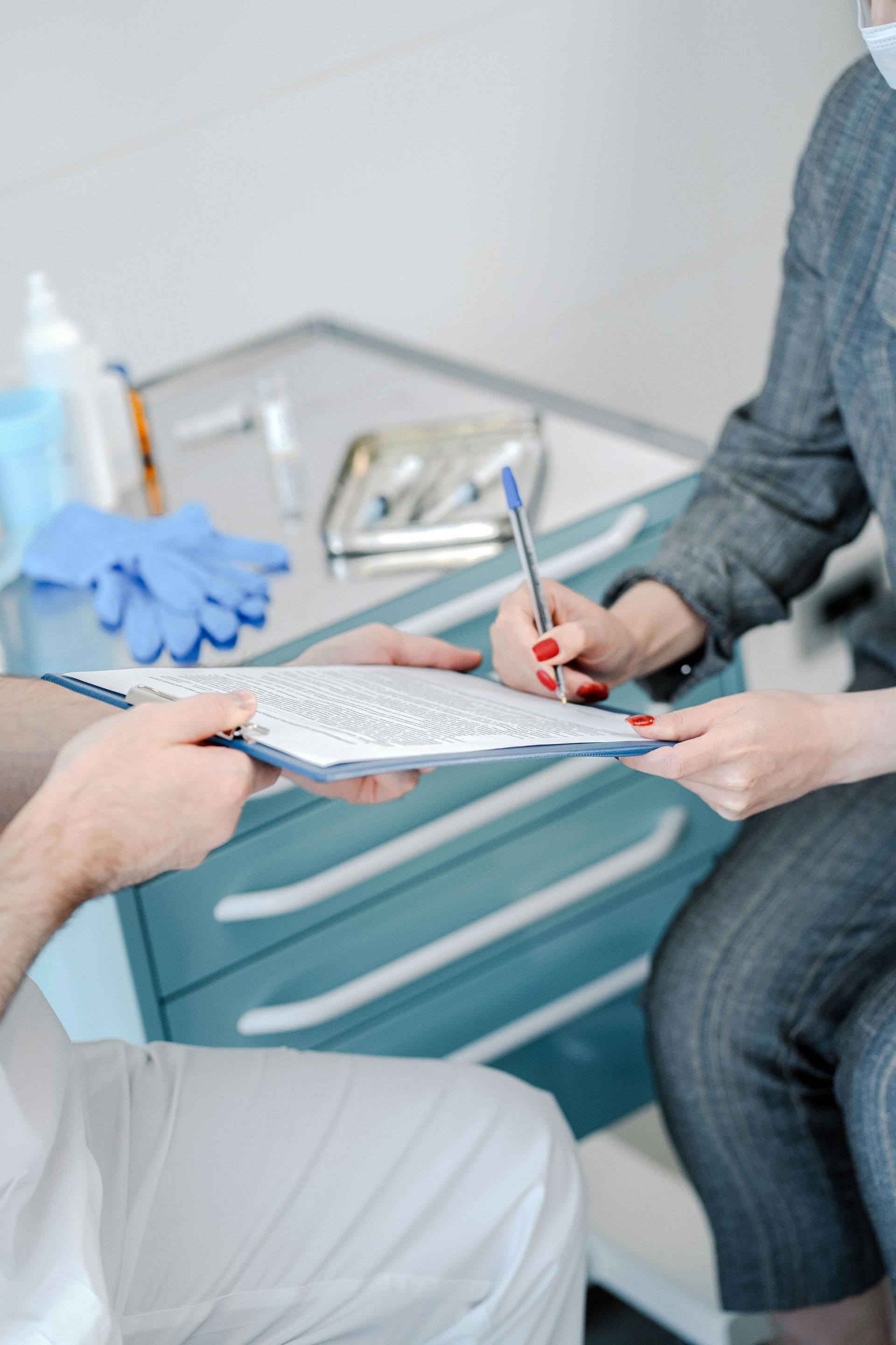 A person in a medical uniform holds a clipboard while another person writes on it in a clinical setting.