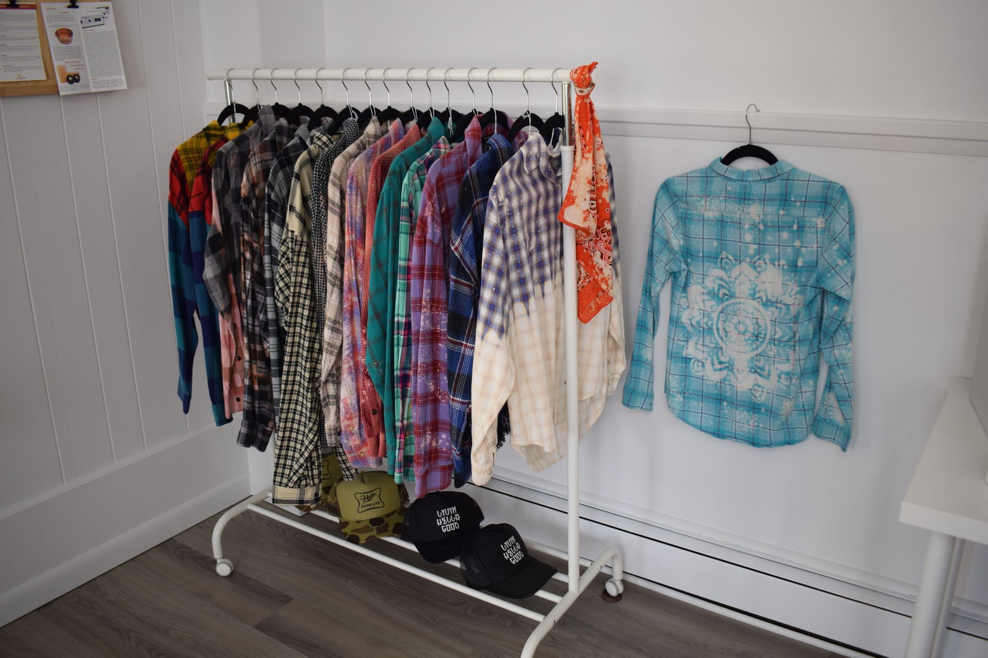 A clothes rack filled with shirts and hats in a room.