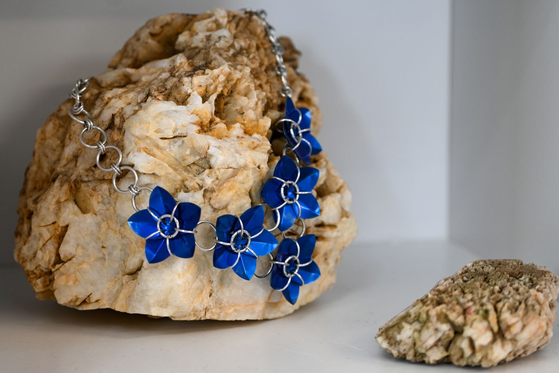 A necklace with blue flowers is sitting on a rock.