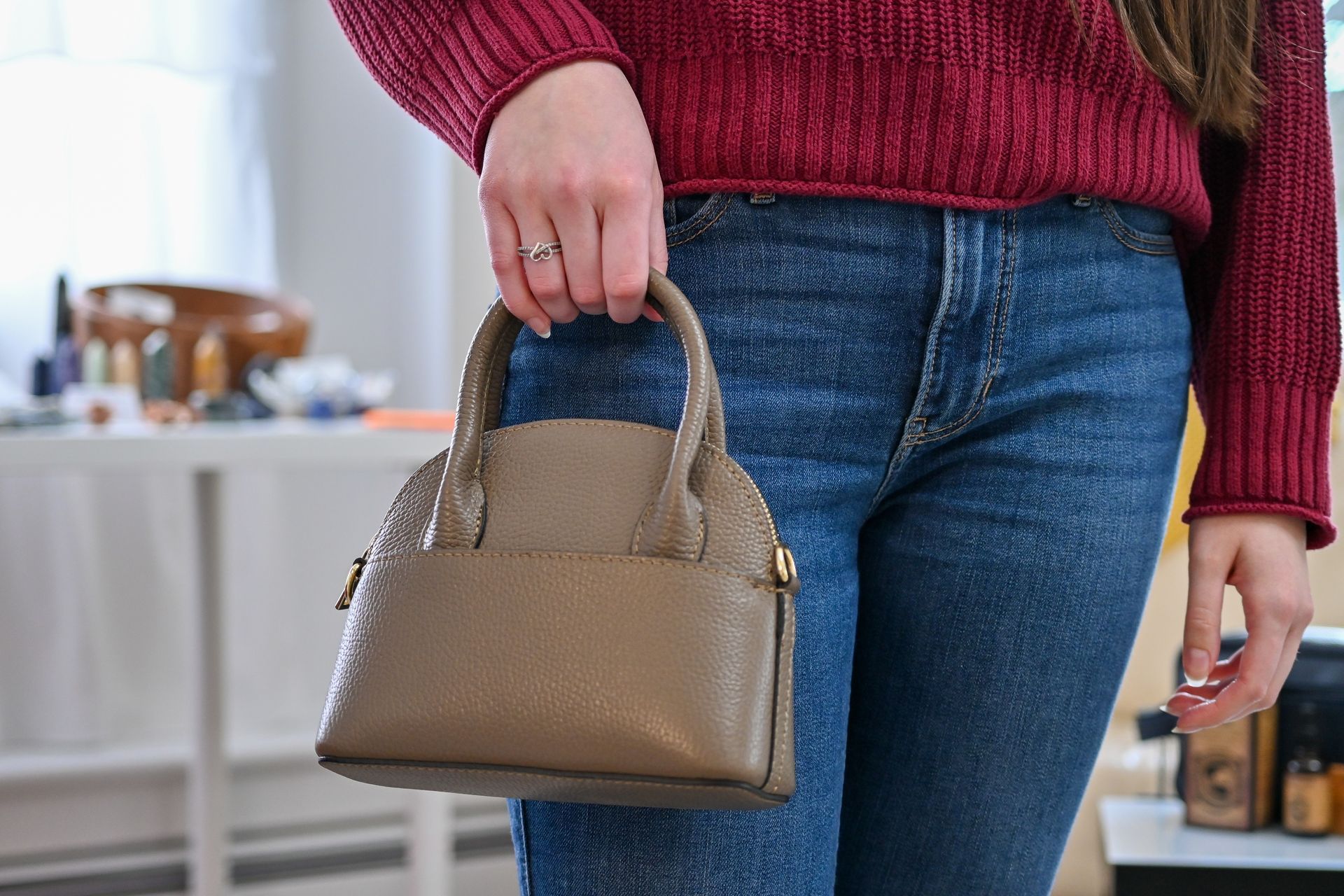 A woman in a red sweater and blue jeans is holding a small purse.