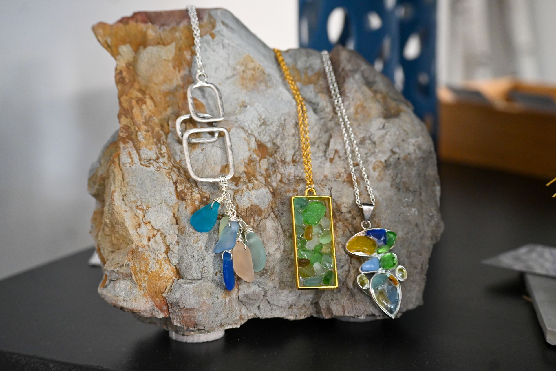 Three necklaces are sitting on top of a rock on a table.