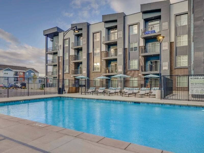 Outdoor rectangular swimming pool with lounge chairs and umbrellas at an apartment complex.