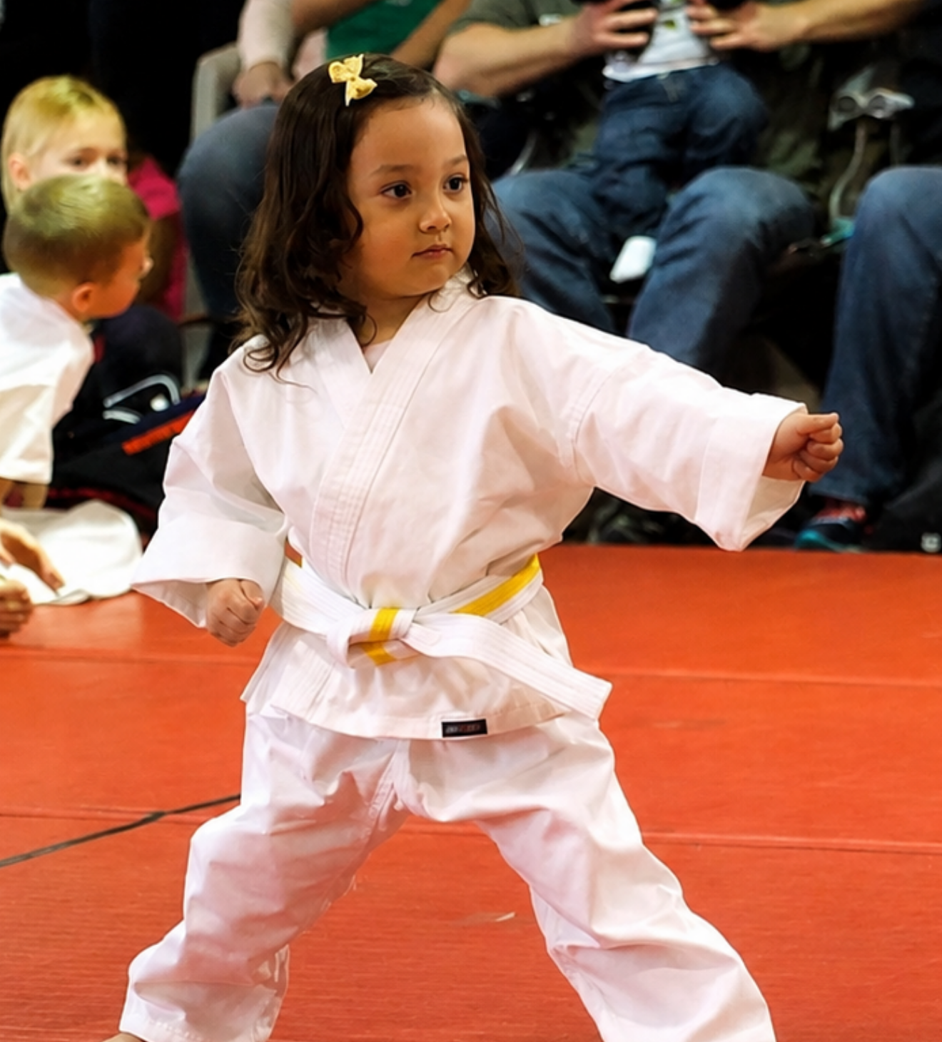 Child in a white martial arts uniform posing on a red mat during a class or competition