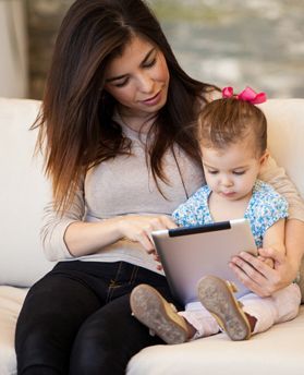 Woman babysitting a toddler and reading a tablet