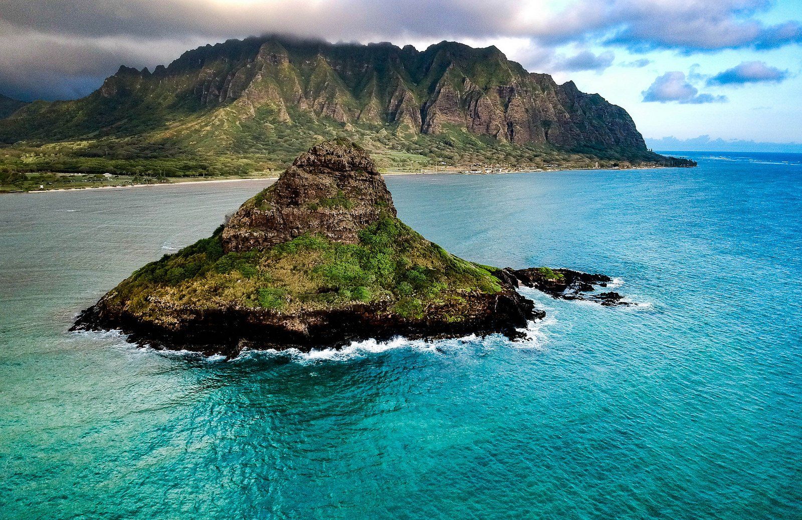 A small island in the middle of the ocean with mountains in the background.