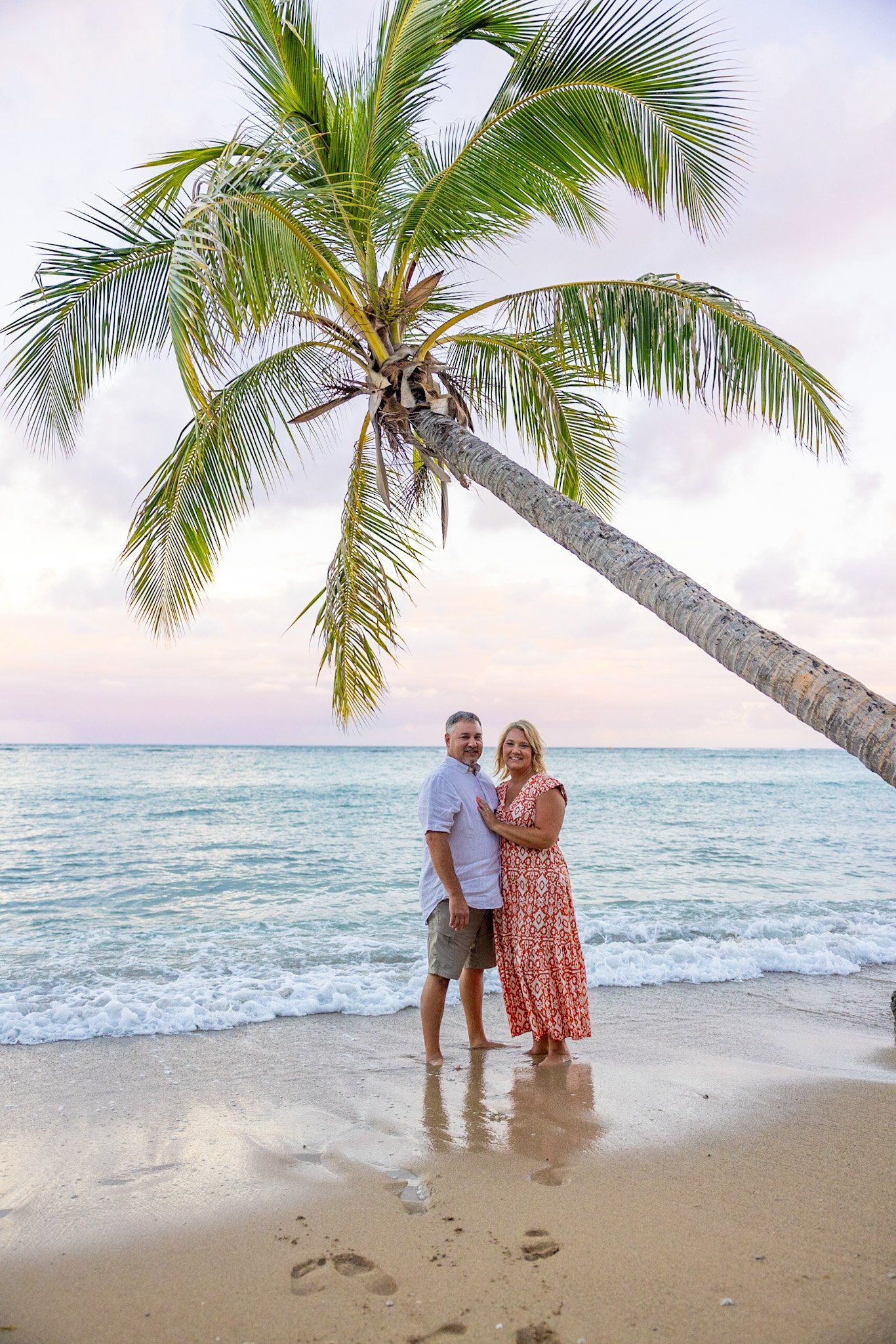 A man and a woman are standing on a beach under a palm tree.