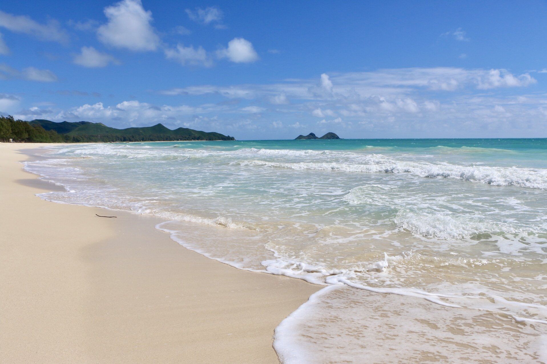 A sandy beach with waves crashing on it on a sunny day.