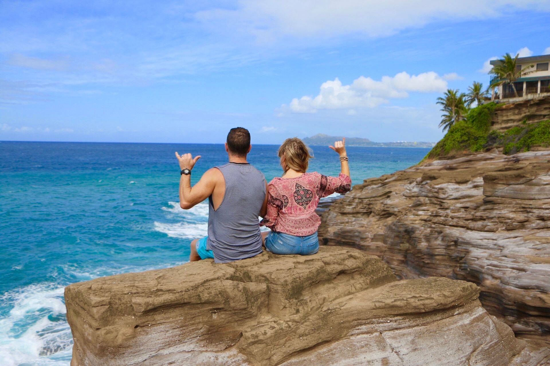 A man and a woman are sitting on a rock overlooking the ocean.