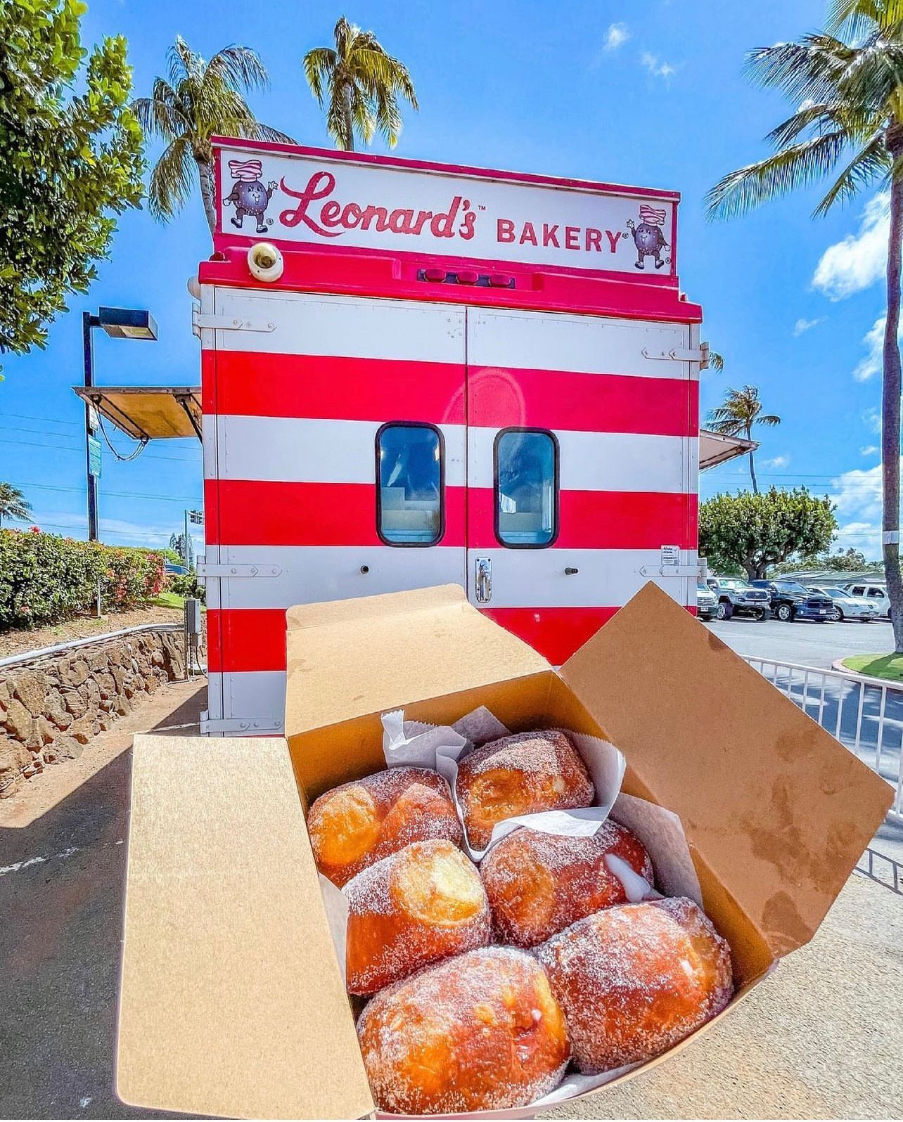 A box of donuts sits in front of a leonard 's bakery truck