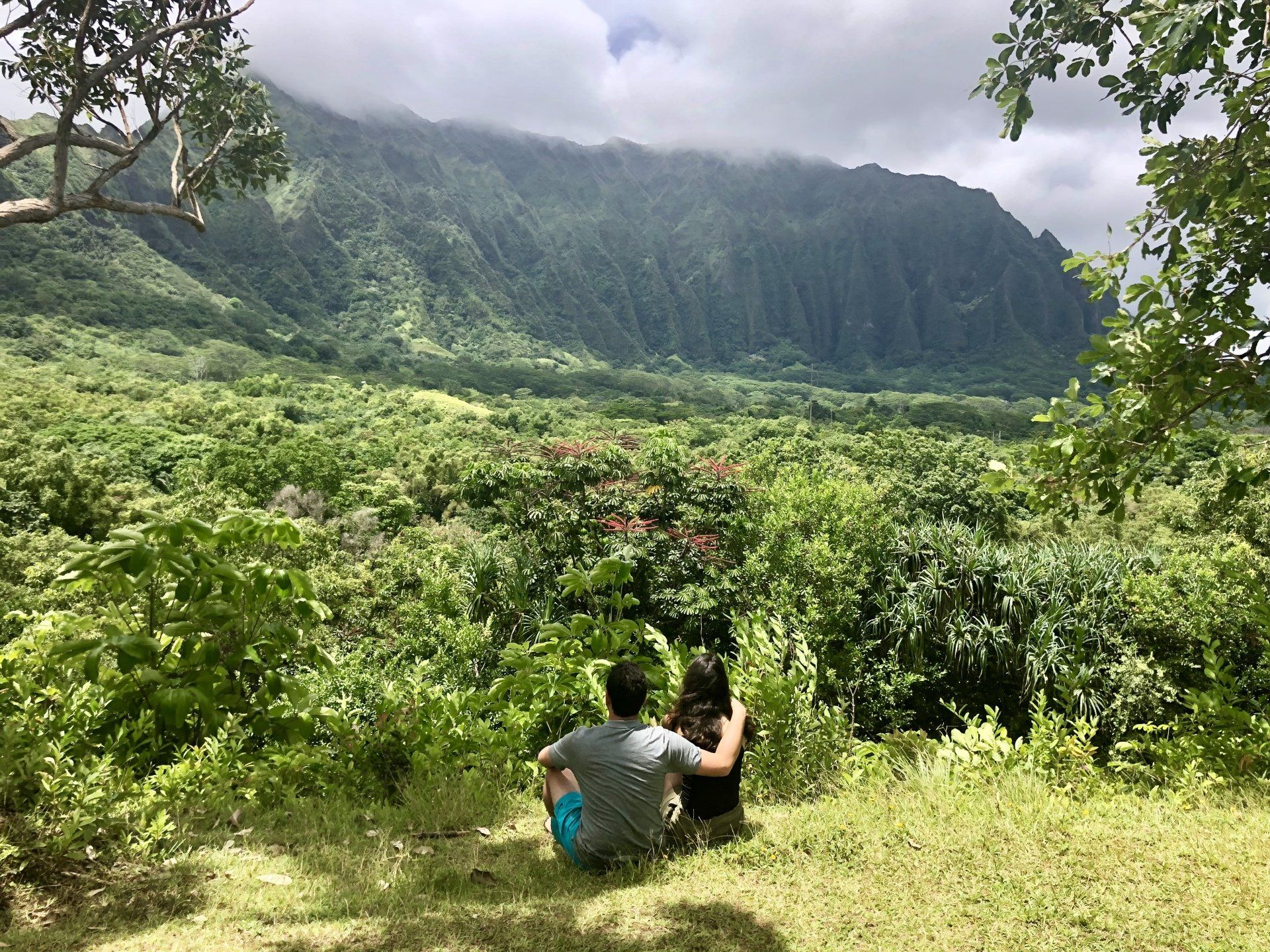 A man and a woman are sitting in the grass looking at a mountain.