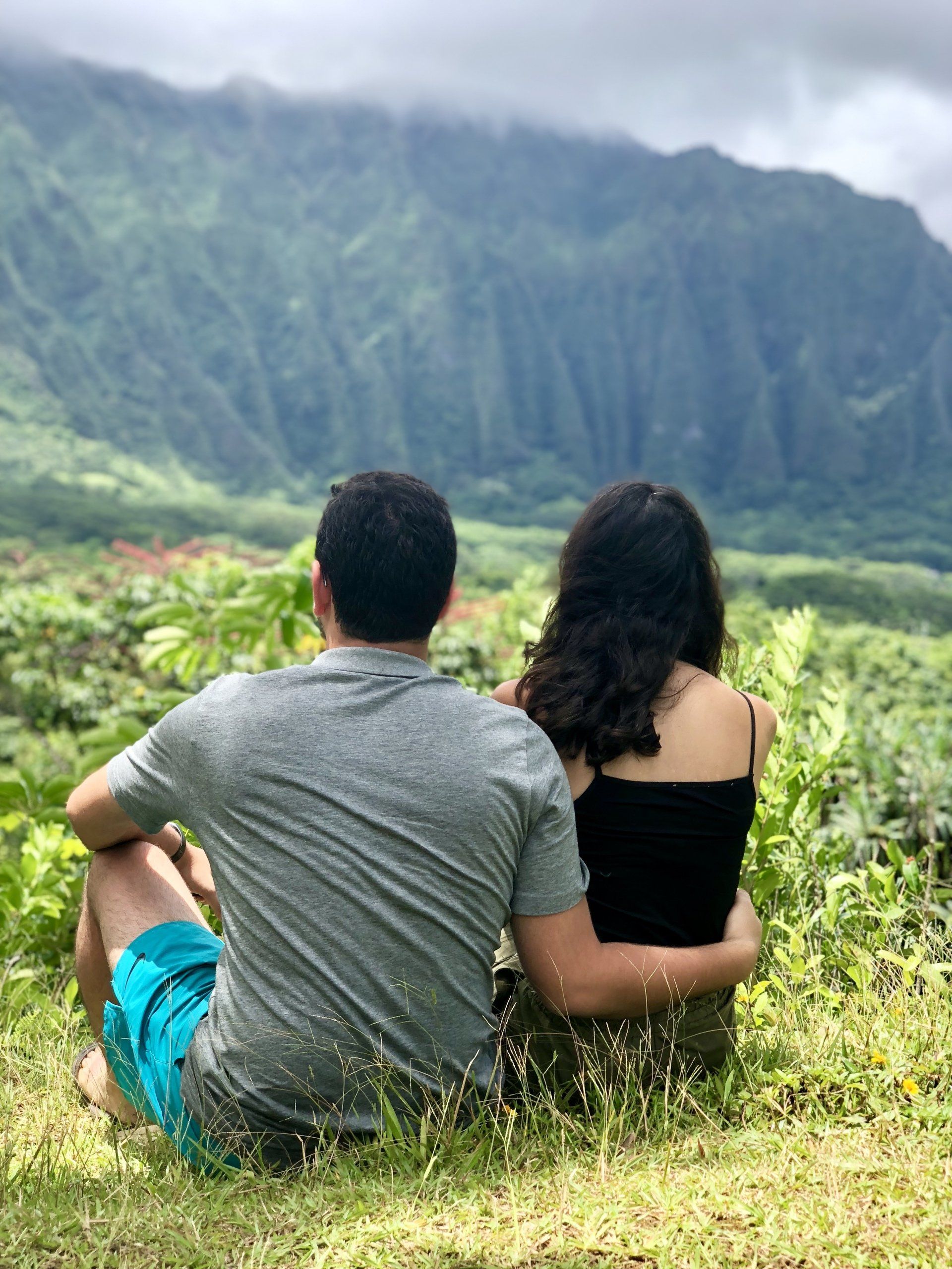 A man and a woman are sitting in the grass looking at a mountain.