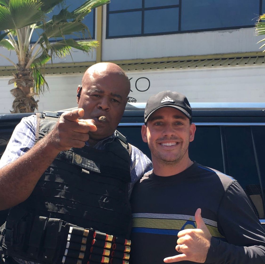 Two men are posing for a picture in front of a building with the letter o on it