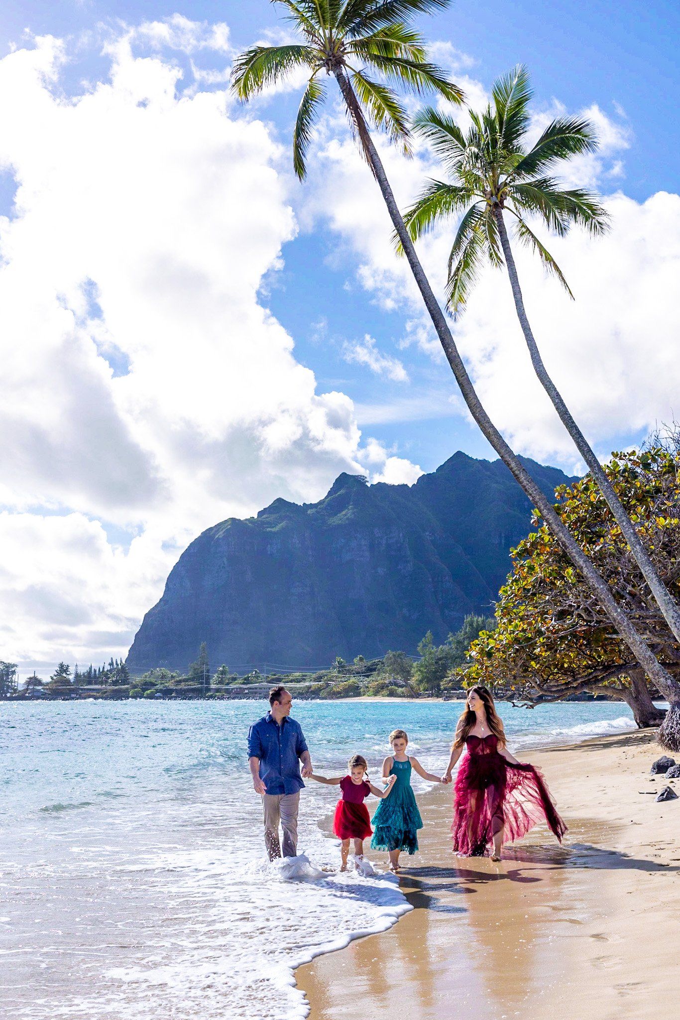 A family is walking along the beach holding hands.