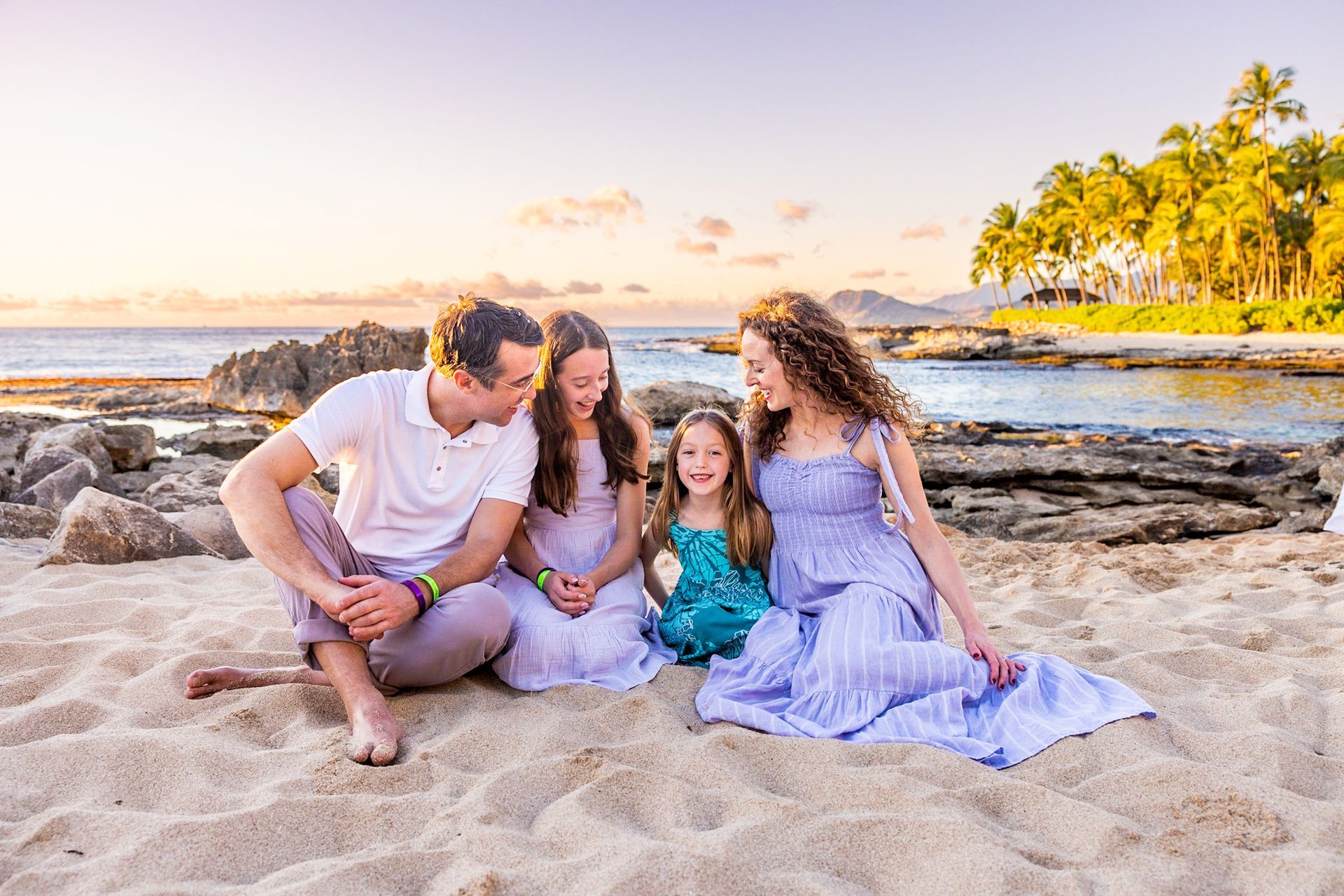 A family is sitting on the beach at sunset.