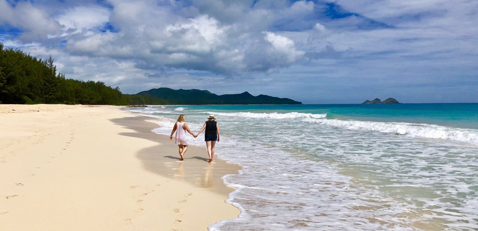 Two women are walking on a beach holding hands.