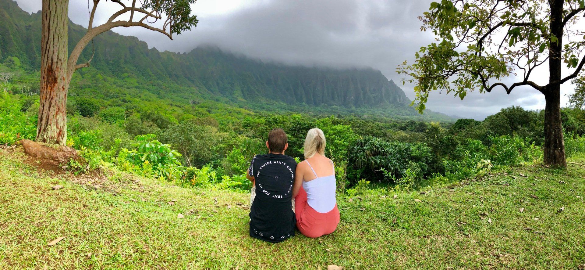 Two people are sitting in the grass looking at a mountain range.