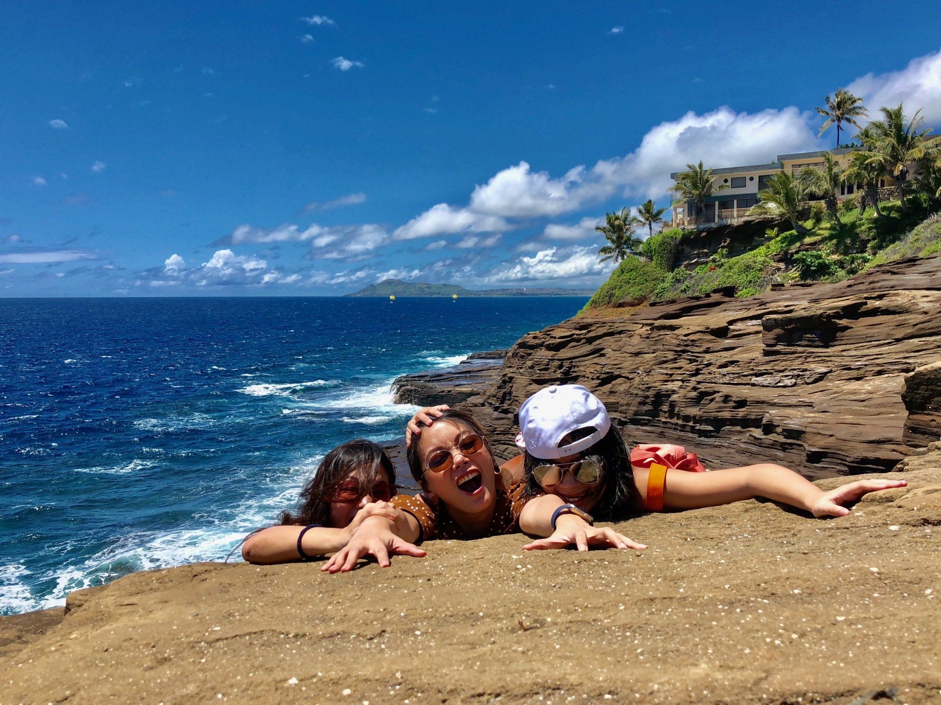 Three people are laying on a rocky cliff overlooking the ocean.