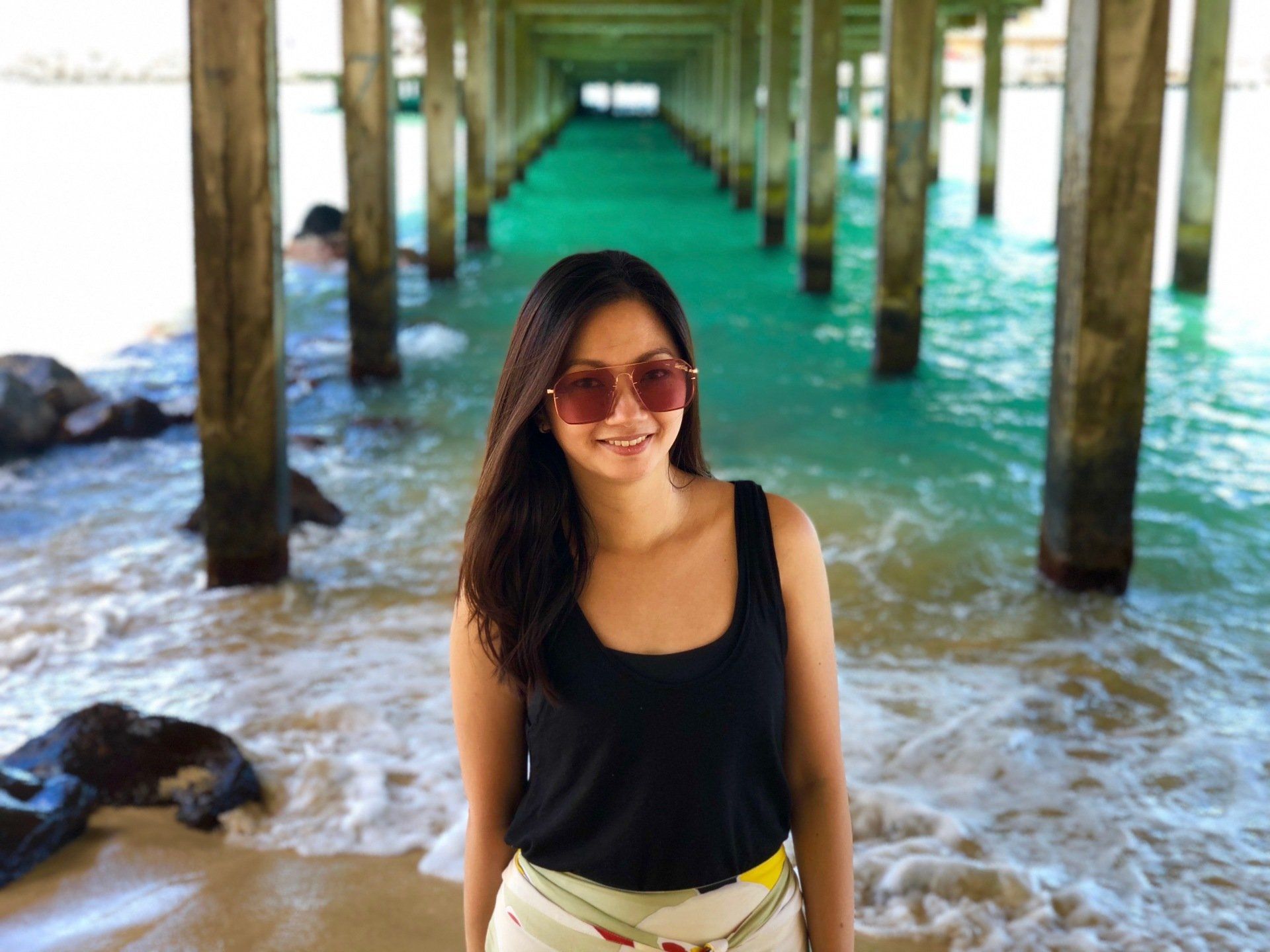 A woman wearing sunglasses is standing under a pier.