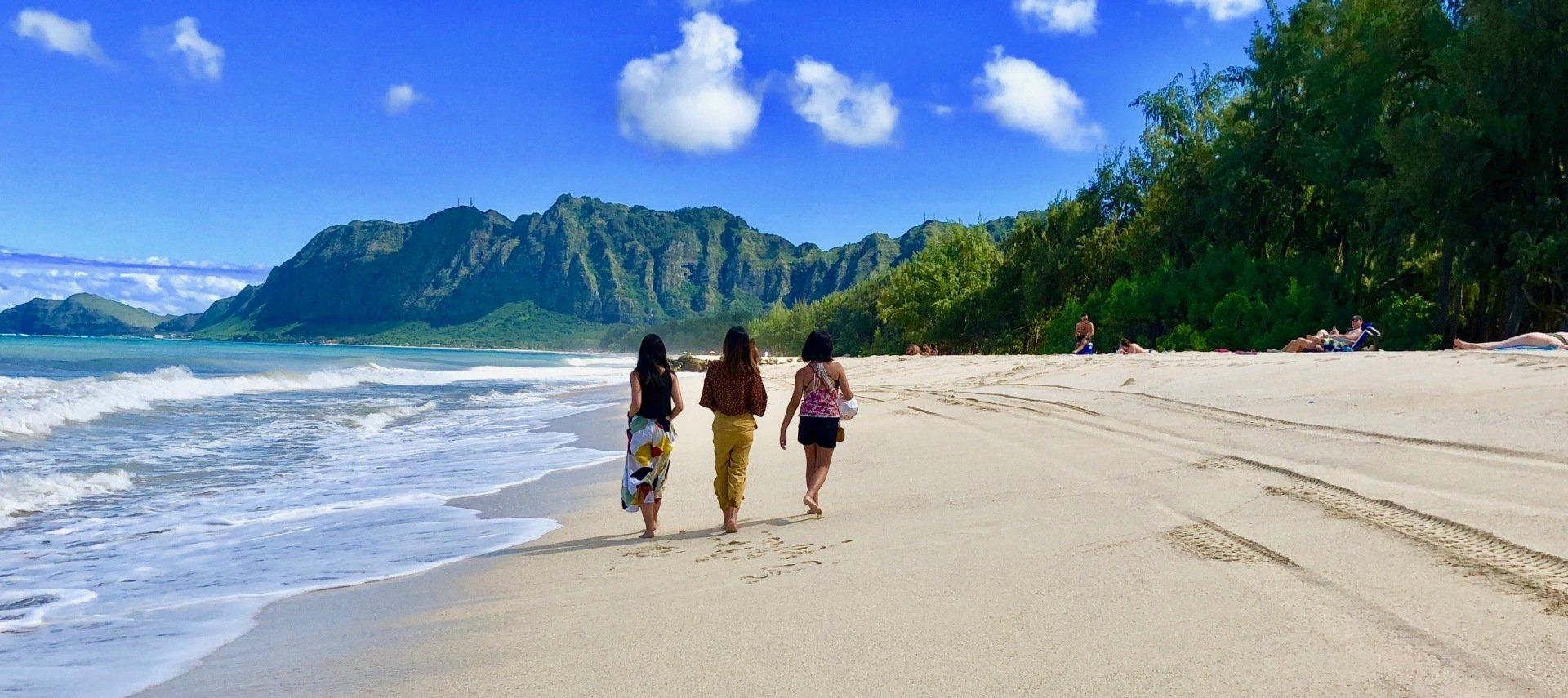 Three women are walking along a sandy beach.