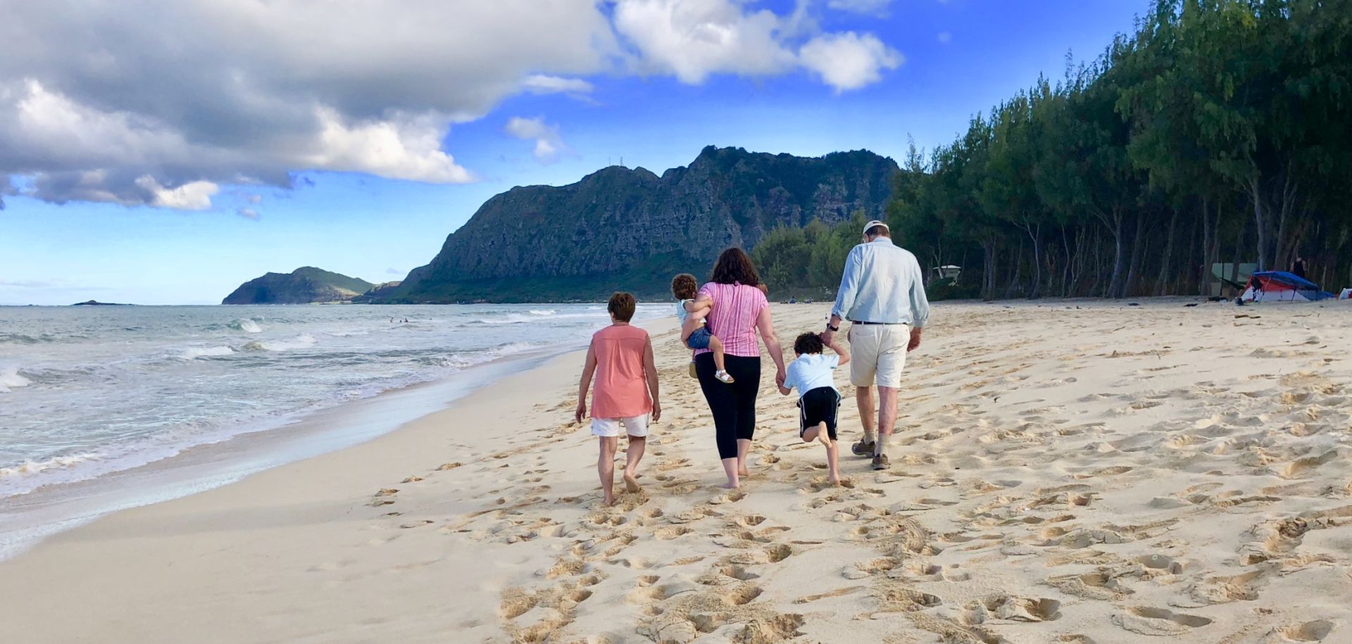 A family is walking on the beach holding hands.