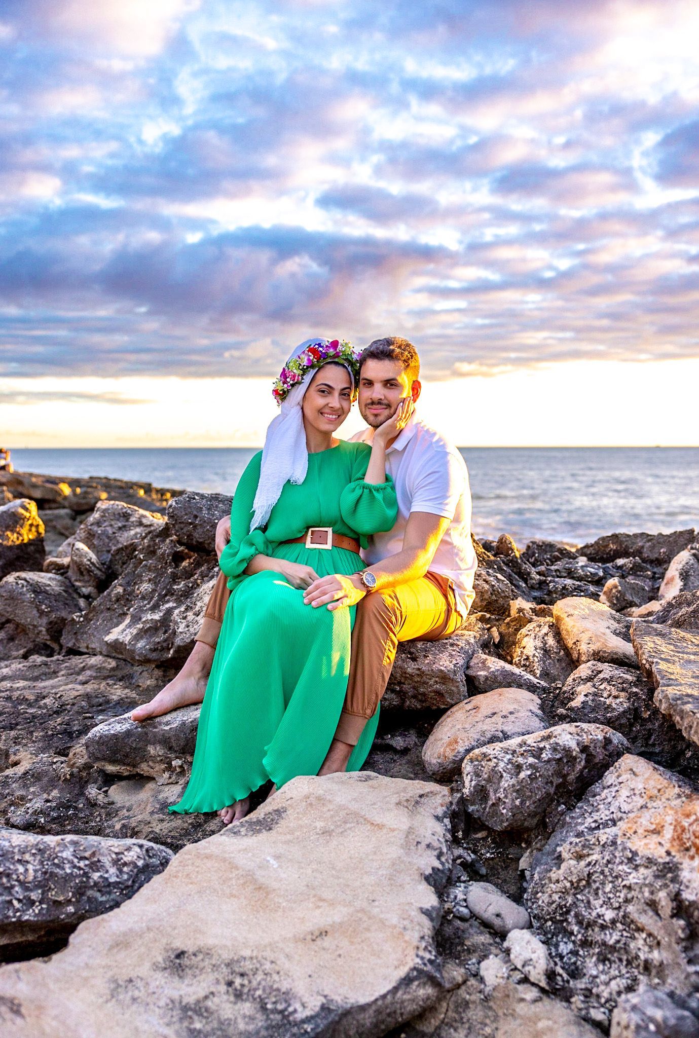 A man and a woman are sitting on rocks near the ocean.