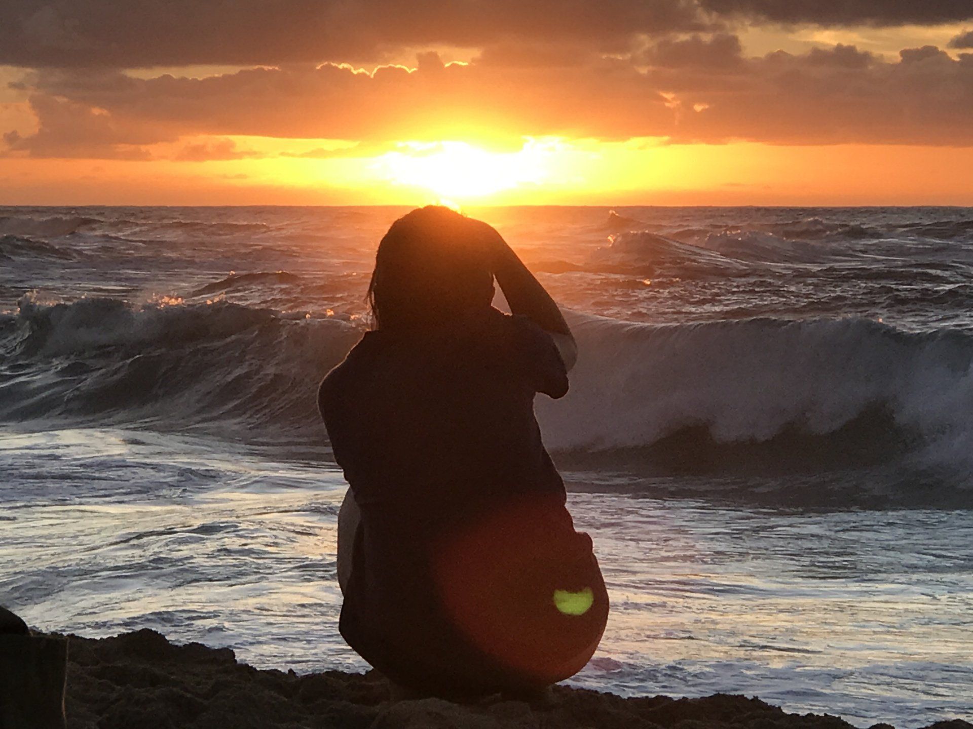 A person is sitting on the beach looking at the sunset