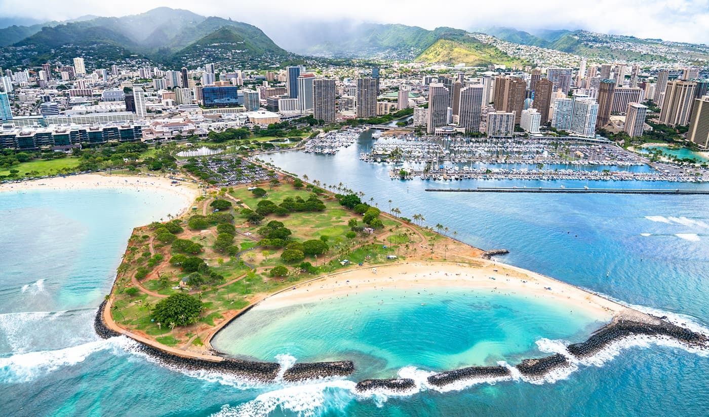 An aerial view of a small island in the middle of the ocean with a city in the background.