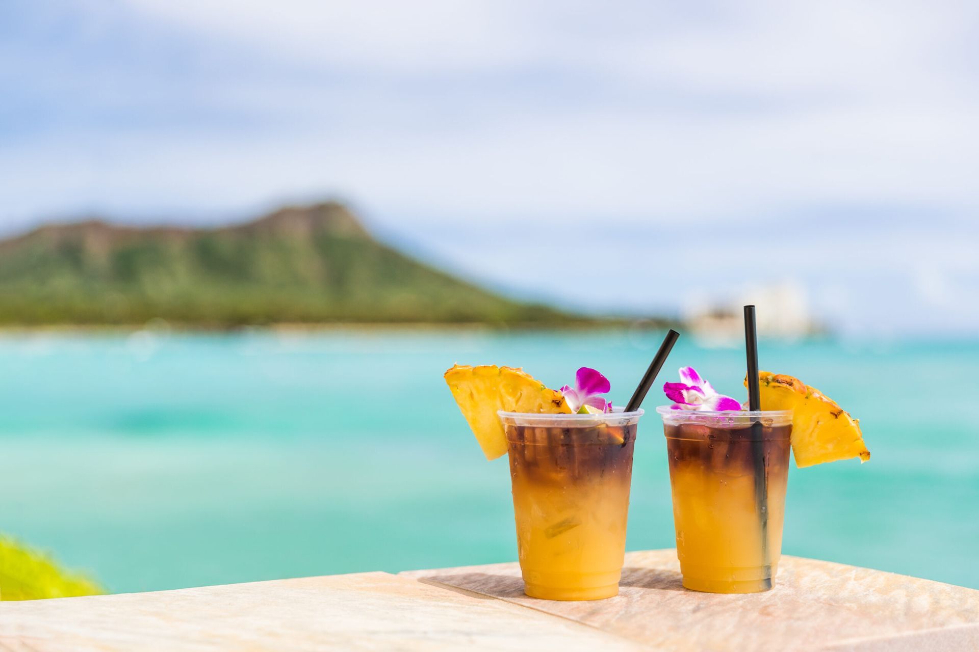 Two drinks are sitting on a table in front of the ocean.